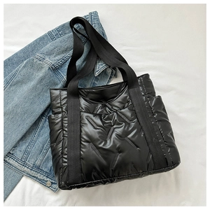 Detail of black quilted puffer tote bag with reinforced straps on blue denim jacket