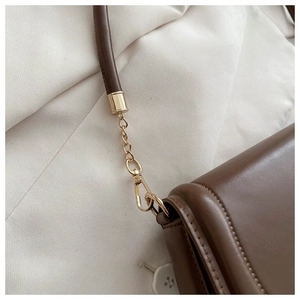 Close-up of the dark brown leather shoulder bag with gold metal buckles and chain links
