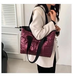 Quilted tote bag in berry purple with black straps shown on a model for scale and fit