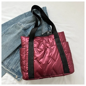 Detail of red quilted metallic tote bag featuring wide black straps and side pocket