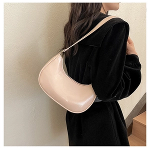 Detail view of glossy beige hobo bag worn with a black coat over the shoulder