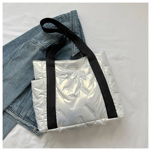 Detail of silver quilted puffer tote bag with black wide straps on white fabric