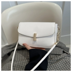 Detailed shot of a white leather crossbody bag with a gold clasp held by a model