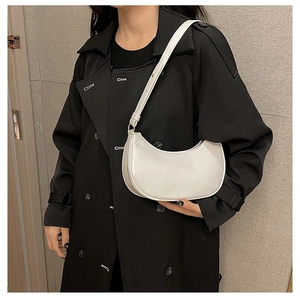 Detailed view of a white minimalist half-moon baguette bag worn over a black trench coat