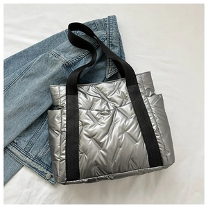 Detail of silver metallic quilted tote bag with black strap on white textured cloth
