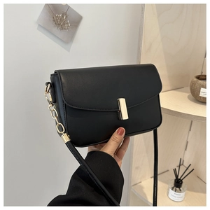 Close-up of black leather shoulder bag with gold metal buckle and chain strap detail
