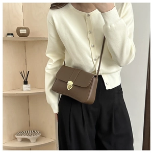 Close-up of brown leather crossbody bag featuring a golden vintage buckle on a model