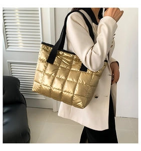 Detail of golden quilted tote bag with wide black straps and metallic finish