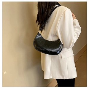 Close-up of a black crescent shoulder bag in glossy patent leather worn by a model