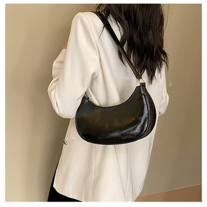 Detail showing high-gloss black crescent underarm bag styled with a white blazer