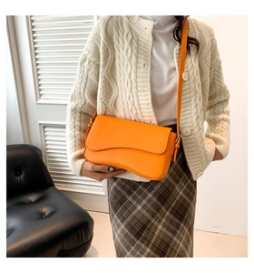 Detail view of the wave-shaped flap and magnetic closure on a bright orange shoulder bag