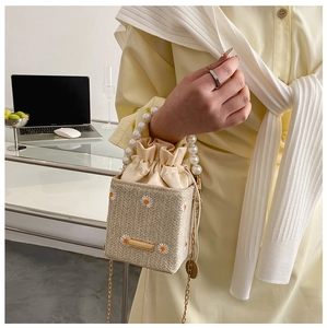 Detail of straw bucket bag with daisy embroidery, pearl handle and gold chain strap