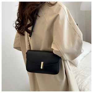 Close-up of minimalist black leather crossbody bag featuring a golden vertical metal clasp