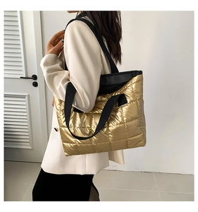 Detail of a large gold quilted tote bag with black strap worn by a model in a white suit