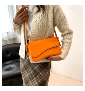 Orange shoulder bag with asymmetric flap styled with beige knitwear and plaid skirt