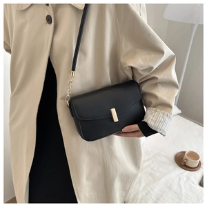 Detail of black leather crossbody bag with gold metal buckle and chain strap on a model