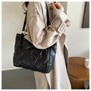 Détail d'un sac cabas matelassé noir avec motif en treillis porté sur un manteau beige