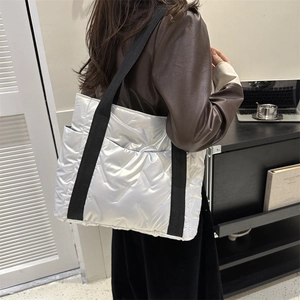 Chic silver quilted puffer tote bag with black straps in a minimalist fashion setting