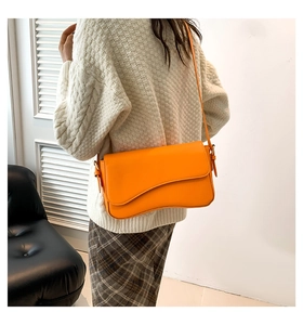 Orange leather flap shoulder bag with wavy asymmetrical design worn by a model