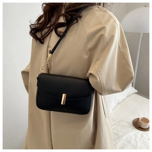 Close-up of minimalist black shoulder bag with elegant gold metal bar buckle and strap detail