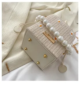 Detail of straw woven handbag with daisy embroidery, pearl handle and protective base studs