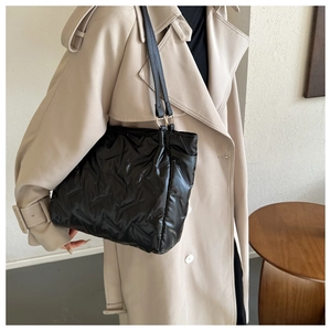 Détail du sac cabas matelassé noir avec anneaux métalliques sur un trench-coat beige