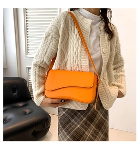 Detail of orange flap crossbody bag with wavy edges worn over a white knit sweater