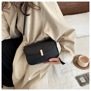 Detail of a vintage black leather crossbody bag with a gold buckle and chain strap