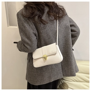 Back view of a model wearing a small white crossbody bag with a gold heart clasp