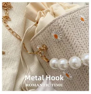Detailed close-up of golden hardware hooks and lace daisy embroidery on a straw bucket bag