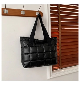 Detail of black quilted tote bag with padded texture hanging in a modern home interior