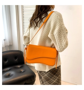 Model wearing orange shoulder bag with unique wavy base and adjustable strap in cozy setting