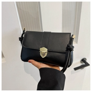 Detail of black leather crossbody bag featuring gold shield clasp and knotted strap detail