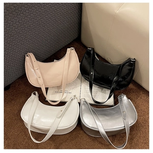 Glossy hobo shoulder bags in beige, black, white, and silver on a plush brown rug