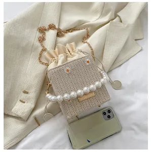 Detail view of woven bucket bag with daisy embroidery, pearl handle, and phone for scale