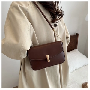 Detail of vintage brown shoulder bag with gold metal clasp on a beige trench coat