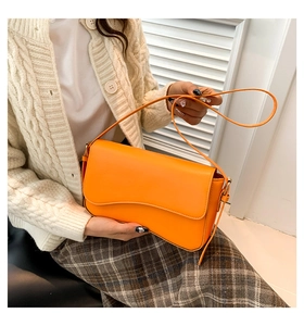 Model wearing a bright orange flap shoulder bag in PU leather with wavy curve design