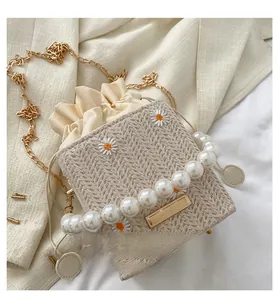 Detail of straw crossbody bag with white daisy embroidery and pearl bead handle
