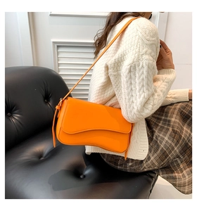 Detail shot of bright orange leather shoulder bag with irregular flap and strap