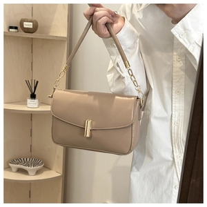Detail of light brown shoulder bag featuring a cylindrical gold clasp and metal chain strap