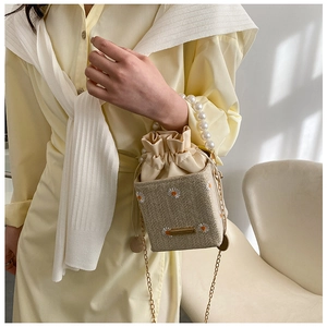 Detailed view of straw bucket bag with daisy embroidery, pearl handle and chain strap