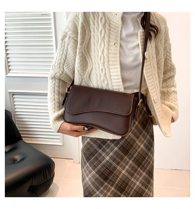 Detail of a dark brown shoulder bag with wavy flap design on a model in natural light