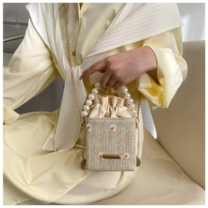 Detail of straw woven bucket bag with pearl handle and daisy embroidery worn by model