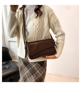 Detail of dark brown saddle bag with magnetic flap, fine stitching and gold hardware