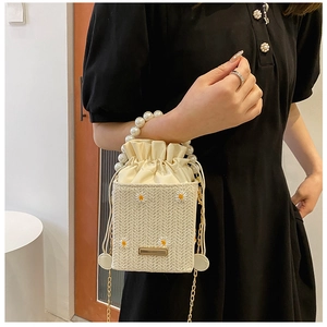 Detail of straw woven bucket bag featuring daisy embroidery and imitation pearl handle