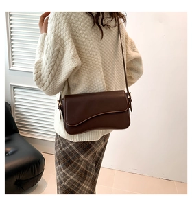 Detail of dark brown leather crossbody bag with wave curve flap and gold buckle