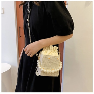 Close-up of beige woven straw bucket bag featuring daisy embroidery and pearl handle