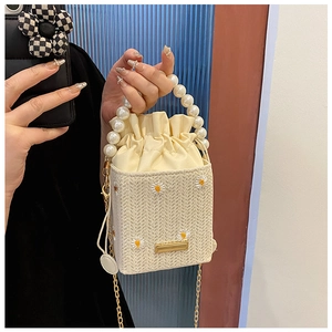 Detailed shot of straw bucket bag with daisy embroidery and large pearl handle