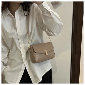 Detail of minimalist leather shoulder bag featuring a sleek gold buckle and metal chain strap