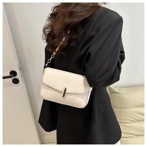 Detail of cream-white leather crossbody bag with gold buckle and chain strap on a model